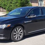 Black Lincoln sedan parked on a residential street with houses and greenery in the background, side view.1