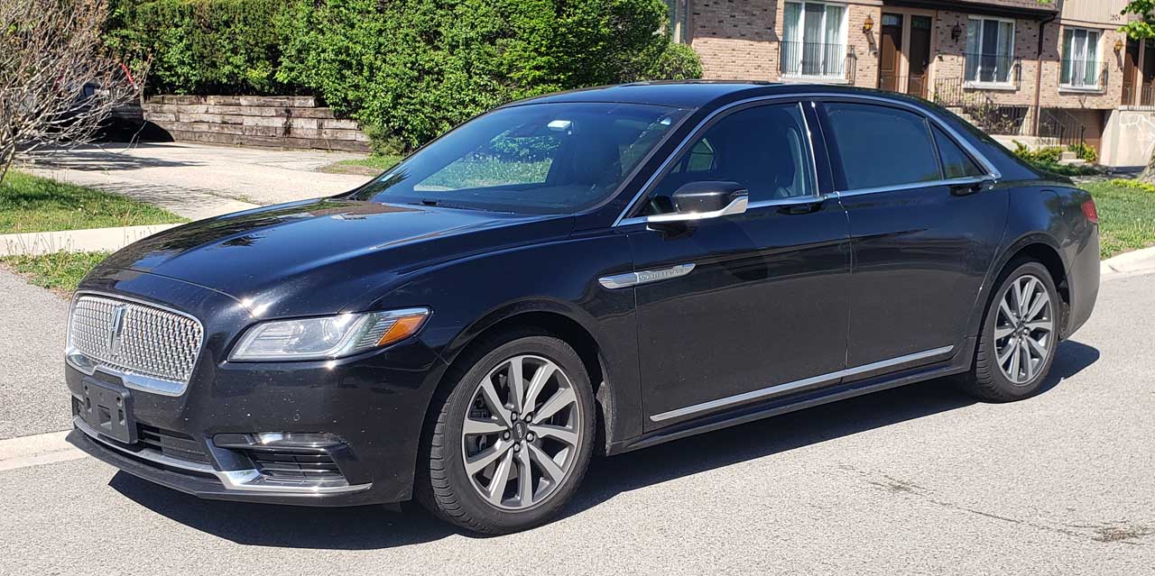 Black Lincoln sedan parked on a residential street with houses and greenery in the background, side view.1