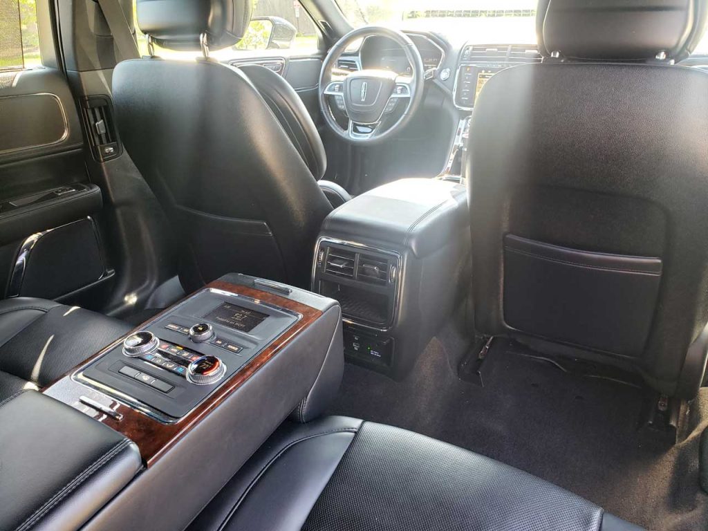 lincoln-continental-passenger-view - Go Chicago Limo Rear passenger area of a luxury SUV with black leather seats and wood-trim center console, climate controls visible in the back.