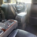 Rear passenger area of a luxury SUV with black leather seats and wood-trim center console, climate controls visible in the back.