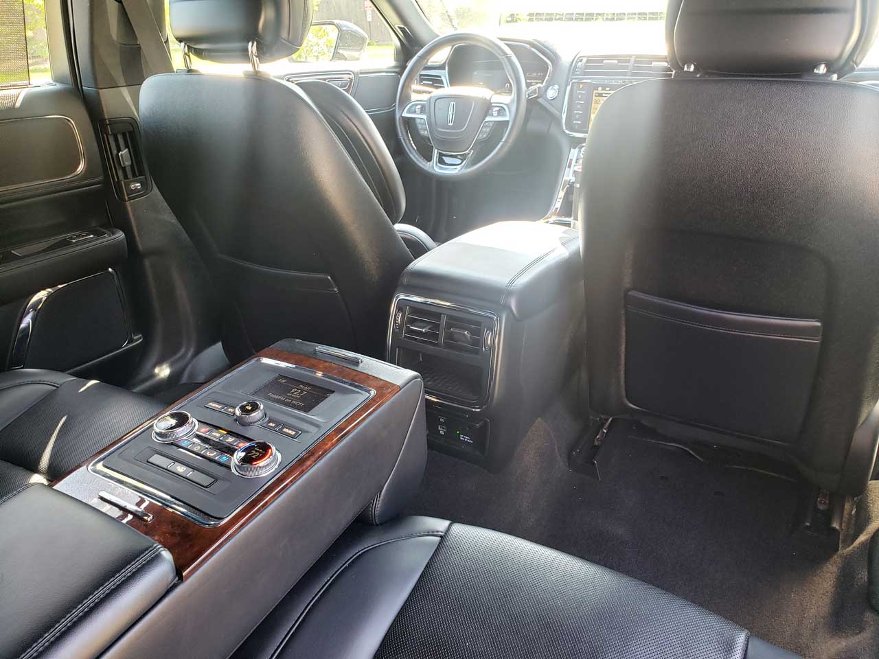 Rear passenger area of a luxury SUV with black leather seats and wood-trim center console, climate controls visible in the back.