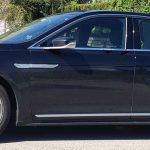 Side view of a black luxury sedan parked on a suburban street, chrome trim and alloy wheels visible.