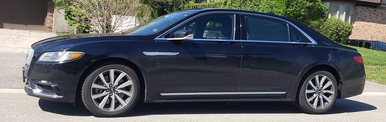 Side view of a black luxury sedan parked on a suburban street, chrome trim and alloy wheels visible.