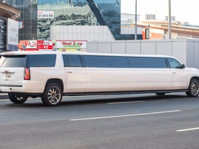 White stretch limousine parked along a city street with modern glass buildings and storefronts in the background.