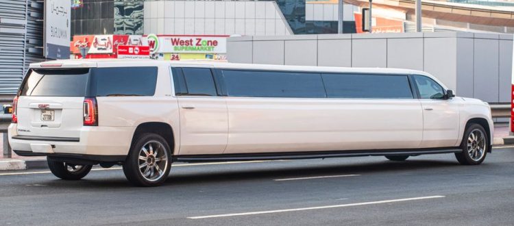 White stretch limousine parked along a city street with modern glass buildings and storefronts in the background.