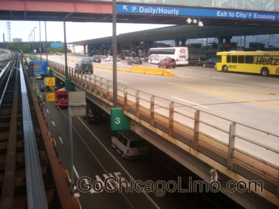 Busy airport roadway with multiple lanes, buses, and cars under a glass terminal canopy; signage shows Daily/Hourly parking and exits to city. GoChicagoLimo watermark on bottom.