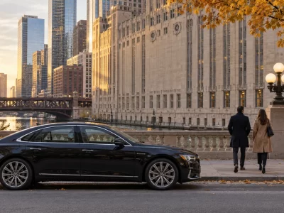 Black sedan beside the Chicago River with two visitors and the opera building beyond