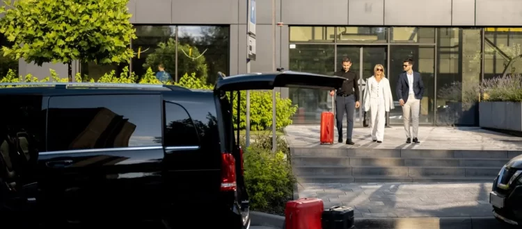 Travelers with luggage beside a black passenger van outside a modern hotel