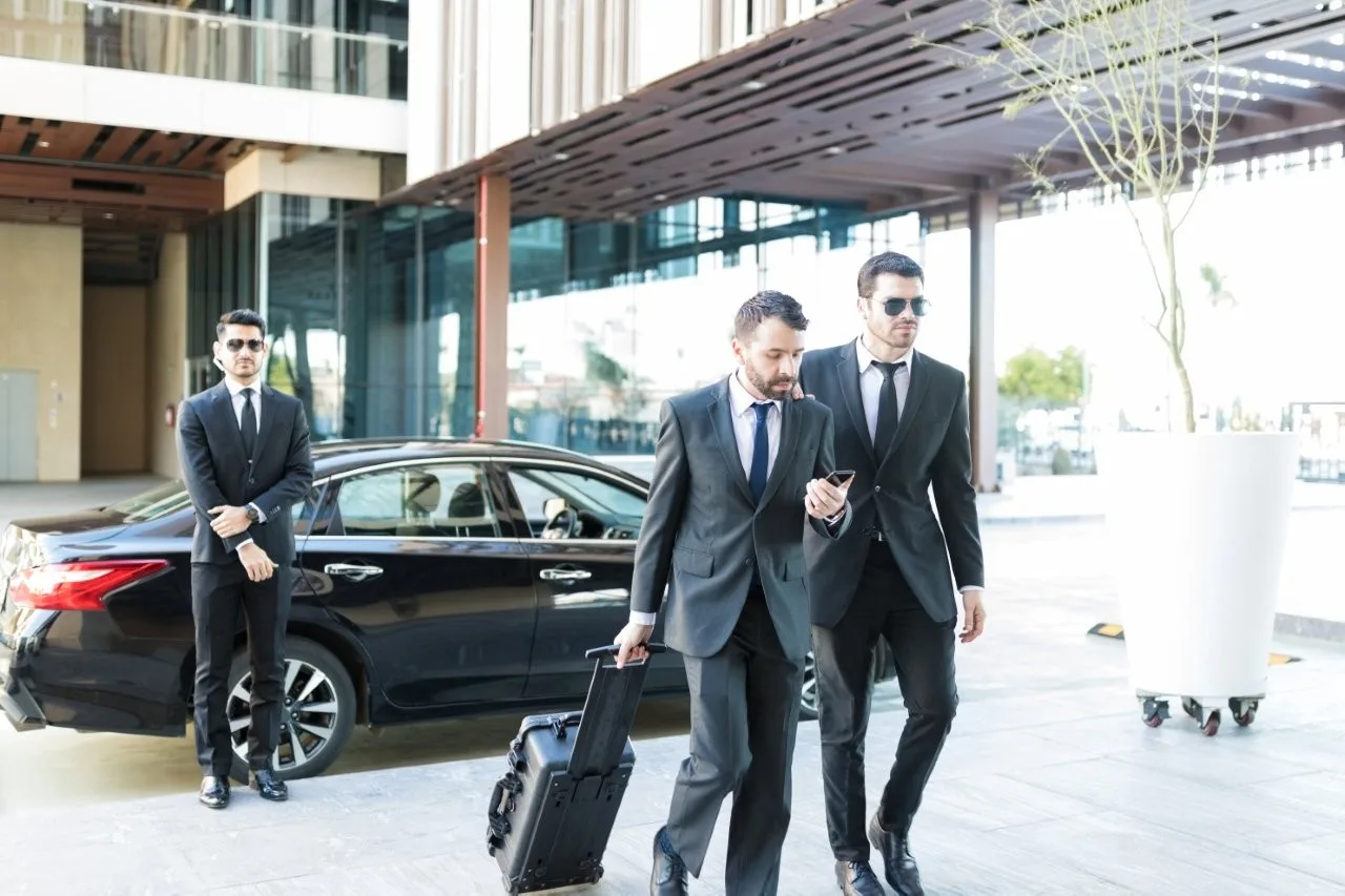 Business travelers beside a sedan - Go Chicago Limo Three men in dark suits beside a black sedan, one pulling a suitcase