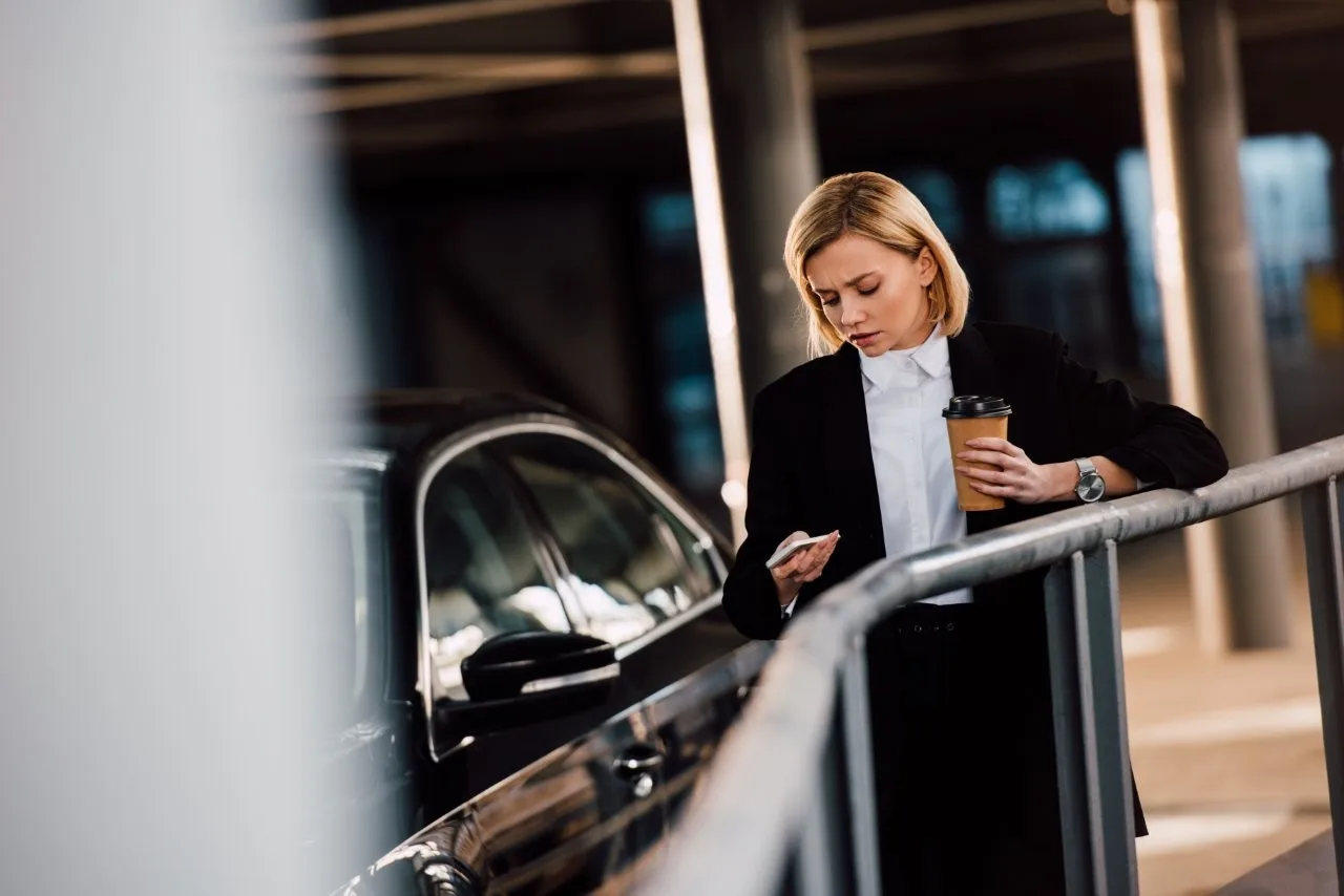 Business traveler beside a car - Go Chicago Limo A woman in a black suit holding a phone and coffee beside a black car and metal railing