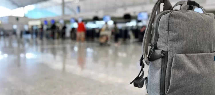 A gray backpack resting on a rolling suitcase inside an airport terminal