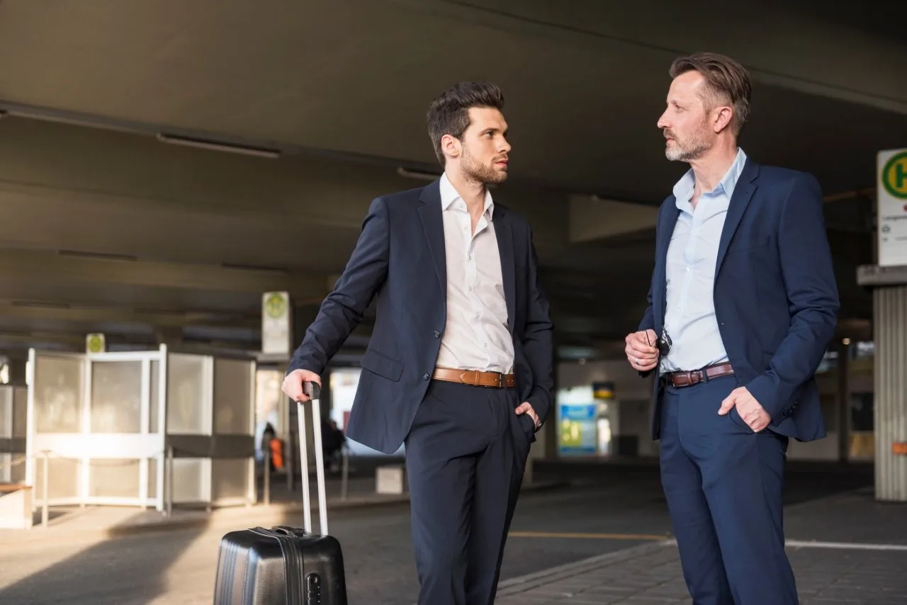 Business travelers talking outdoors - Go Chicago Limo Two men in suits talking under a covered exterior area with a suitcase beside them