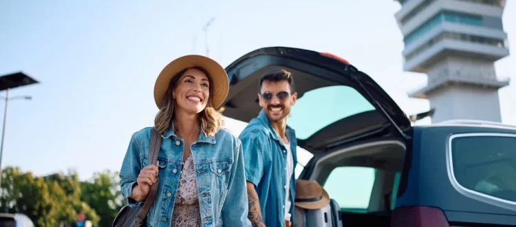 A couple beside an open car luggage compartment near an airport terminal