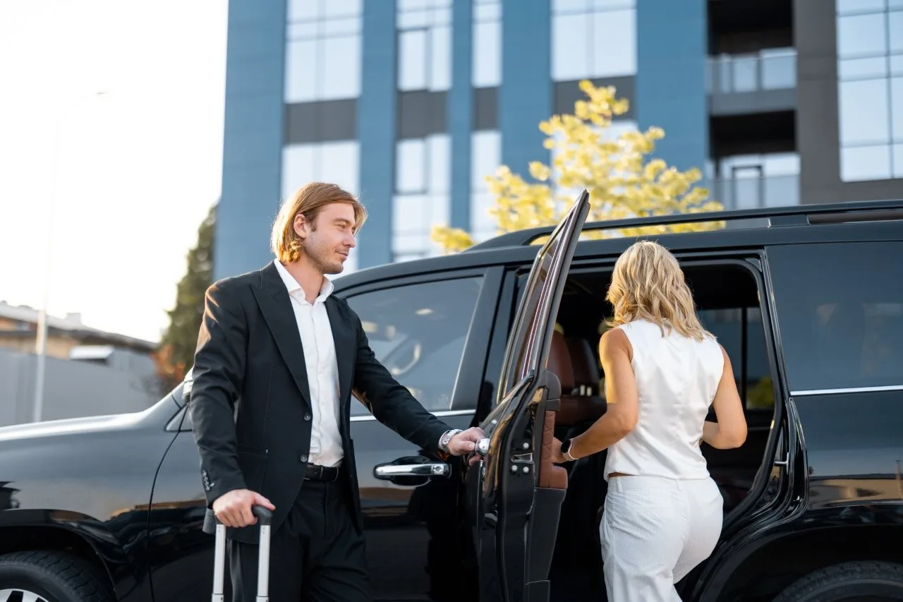 Arrival outside a business destination - Go Chicago Limo A man holding a door as a woman enters a black vehicle outside a modern building